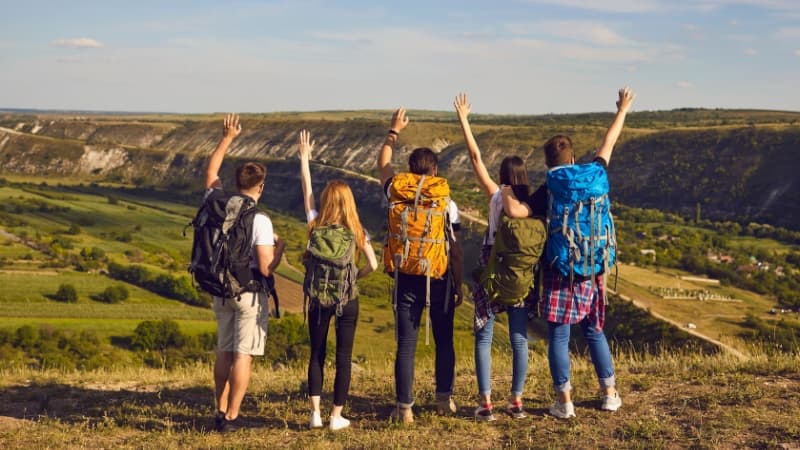 Junge Menschen mit Wanderrucksäcken in einer grünen Landschaft